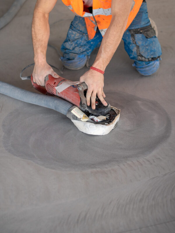 Worker working on the floor of an industrial building. Construction worker producing grout and finishing wet concrete floor.